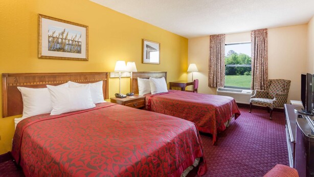 Een hotelkamer met twee bedden, een televisie, een stoel en een raam met gordijnen.