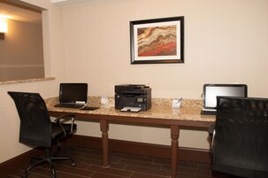 Uma sala de conferências com uma mesa de granito, dois laptops, uma impressora e duas cadeiras de escritório pretas.