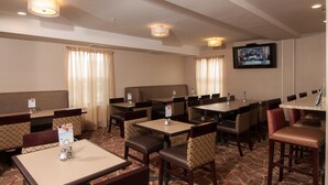 A hotel dining area with multiple tables and booths, ceiling lights, and a television screen.