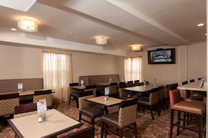 Uma sala de jantar de hotel com várias mesas e cabines, luminárias no teto e uma tela de televisão.