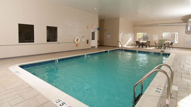 An indoor swimming pool with clear water, tiled edges, and a lifeguard chair. There are chairs and tables near the pool, and a door leading to another room. - Holiday Inn Express Vernon - Manchester by IHG (Vernon)