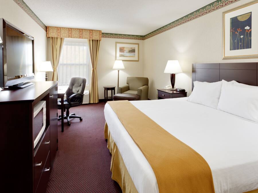 A hotel room with a bed, desk, chair, and a television.