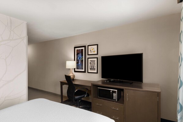A hotel room with a bed, a desk with a chair, a flat-screen TV, a microwave, and framed pictures on the wall.