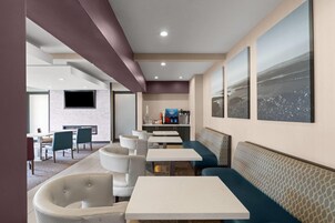 Un interior de restaurante moderno con mesas blancas, asientos tipo banca en azul y una zona de bar.