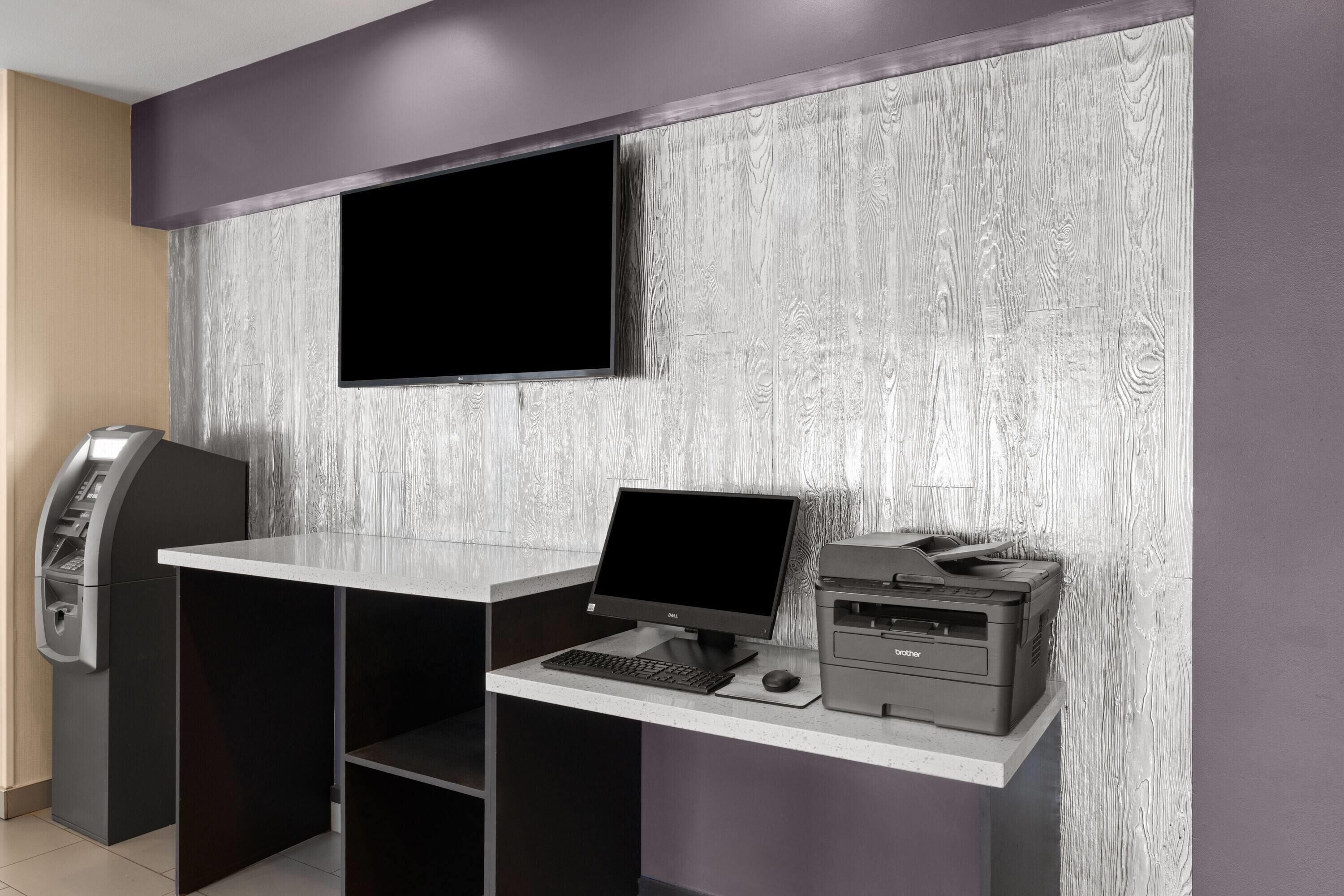 Ein moderner Arbeitsplatz mit Flachbildschirm, Desktop-Computer, Drucker und Telefon an einem Schreibtisch vor einer strukturierten Wand.