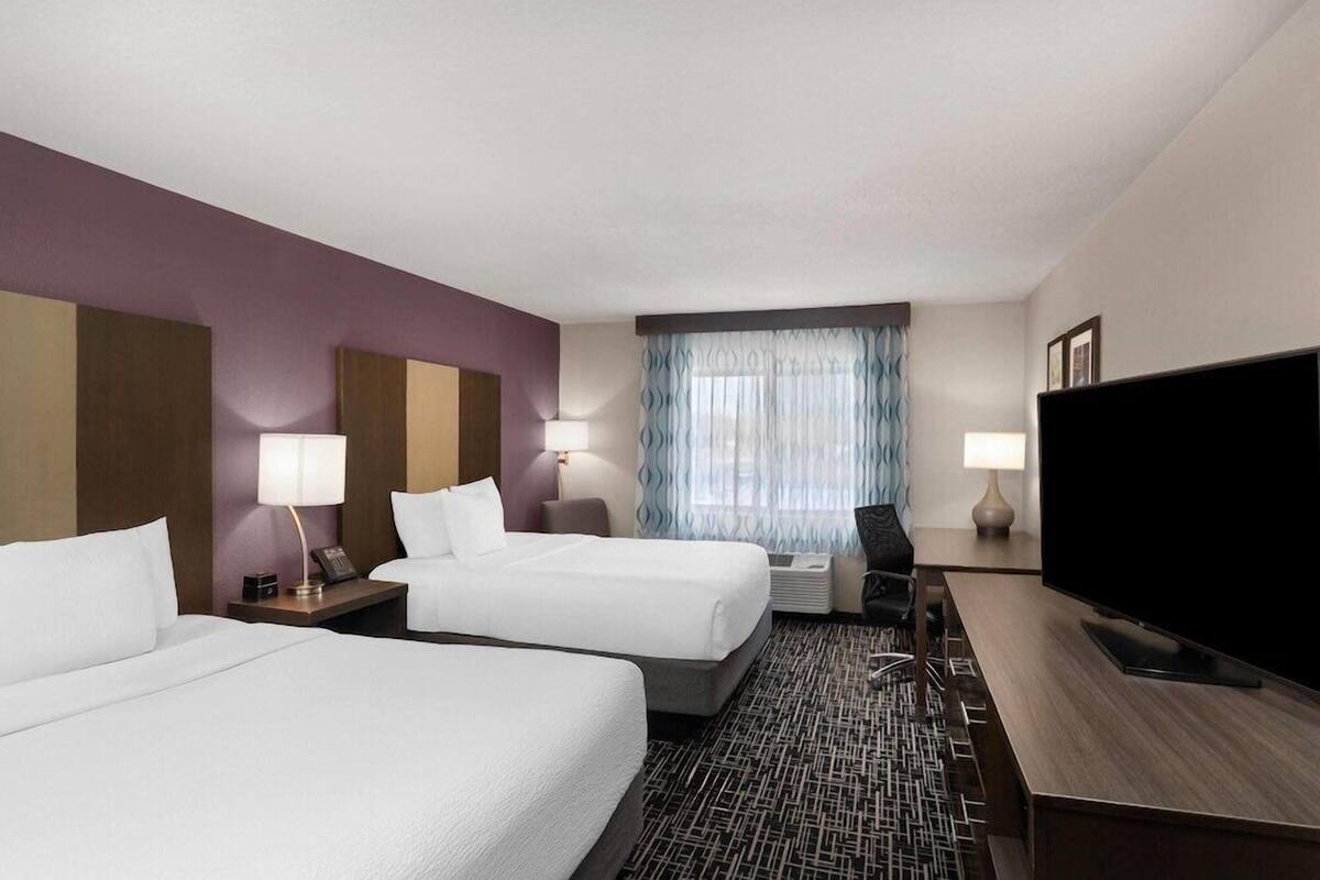 Une chambre d’hôtel avec deux lits, un bureau, une télévision et une fenêtre avec des rideaux.