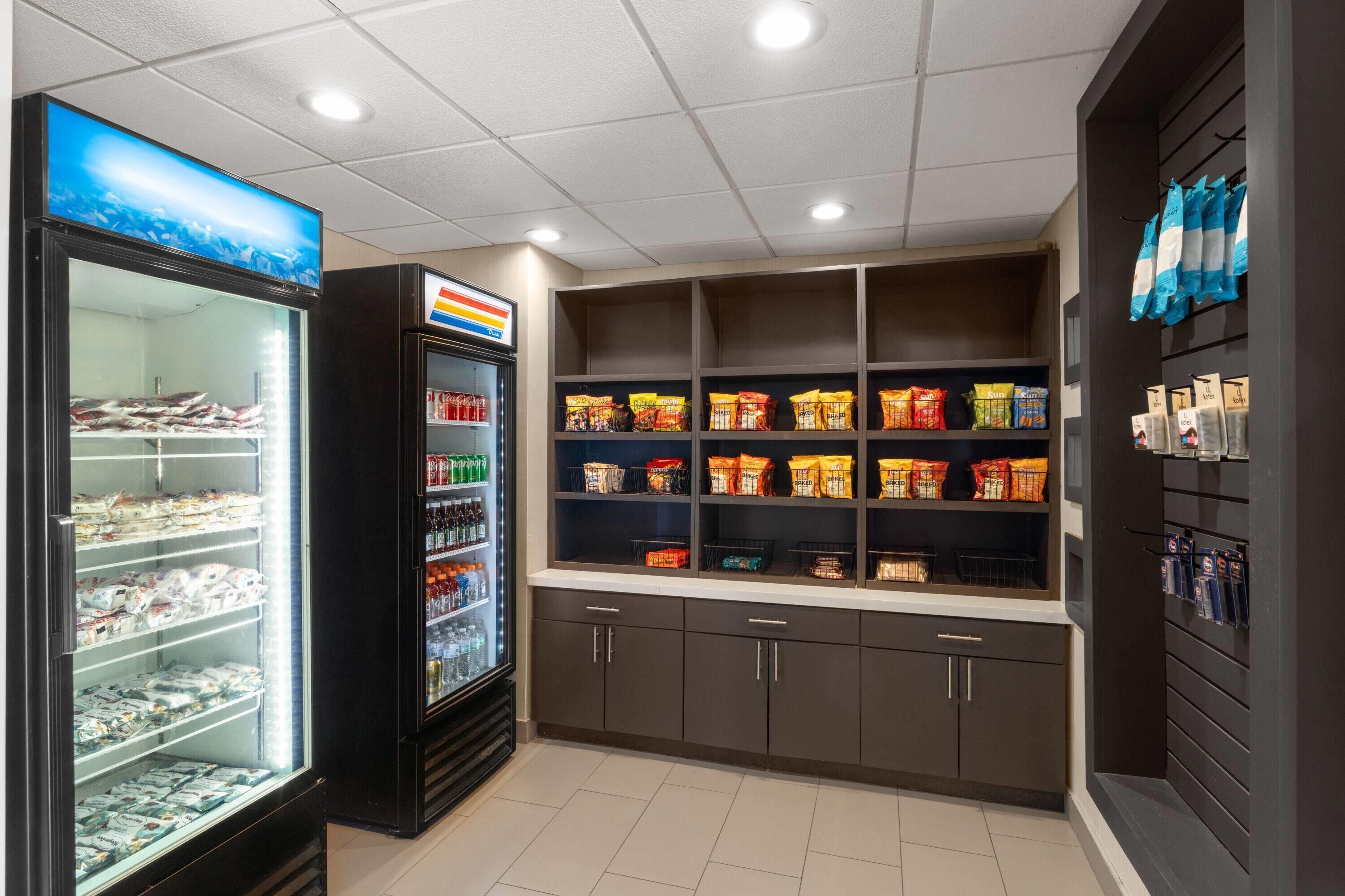 Un expositor refrigerado con diversos productos envasados, una estantería con aperitivos y una vitrina mural con agua embotellada.