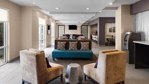 Un hall d’hôtel moderne, doté d’un canapé, de fauteuils, d’un téléviseur et d’un kiosque en libre-service.
