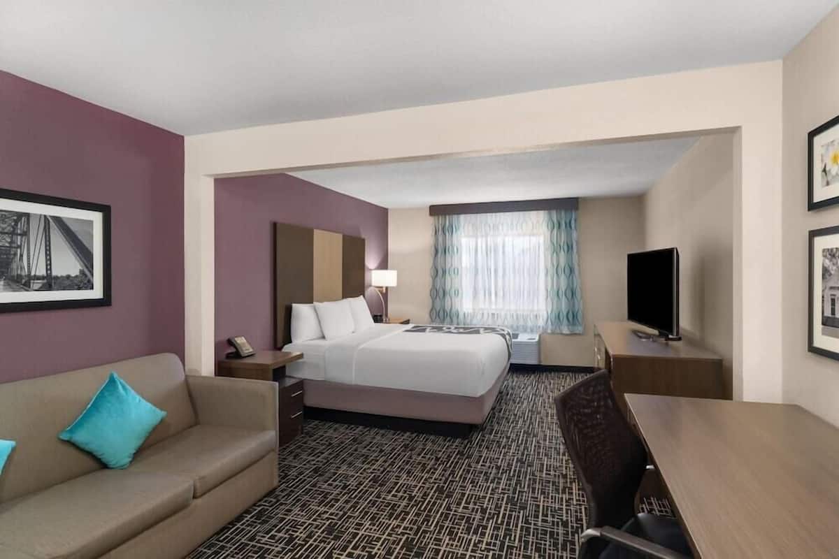 Une chambre d’hôtel avec un lit, un bureau, une chaise, une télévision et une fenêtre avec des rideaux.