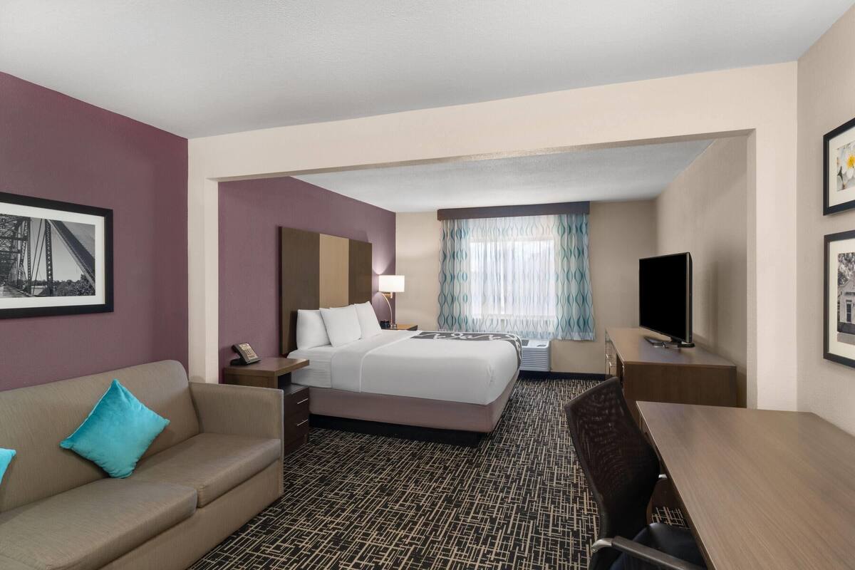 Une chambre d’hôtel équipée d’un lit, d’un bureau, d’une chaise, d’une télévision et d’une fenêtre avec des rideaux.
