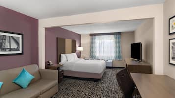 A hotel room with a bed, a desk, a chair, a television, and a window with curtains.