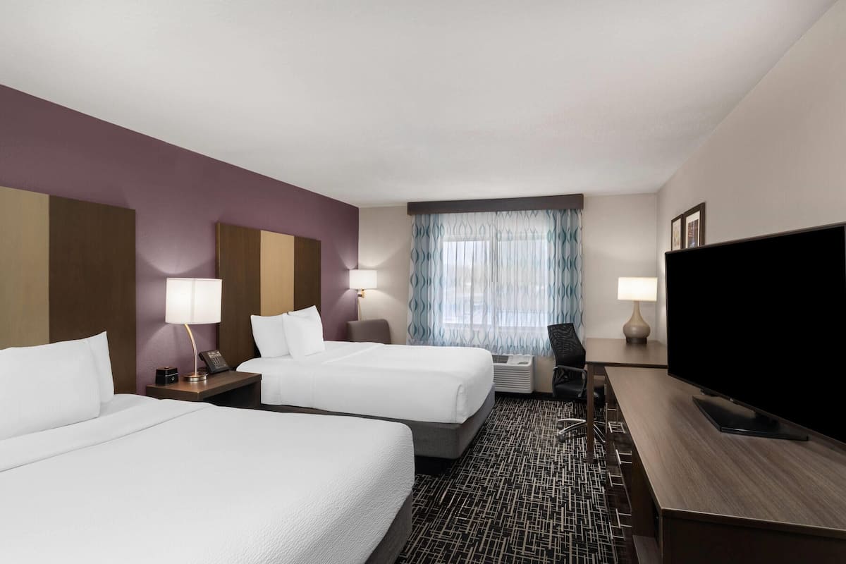 Une chambre d’hôtel avec deux lits, un téléviseur à écran plat, un bureau et une fenêtre avec des rideaux.