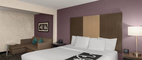 A hotel room with a bed, a sofa, a small table, a nightstand, and a lamp.