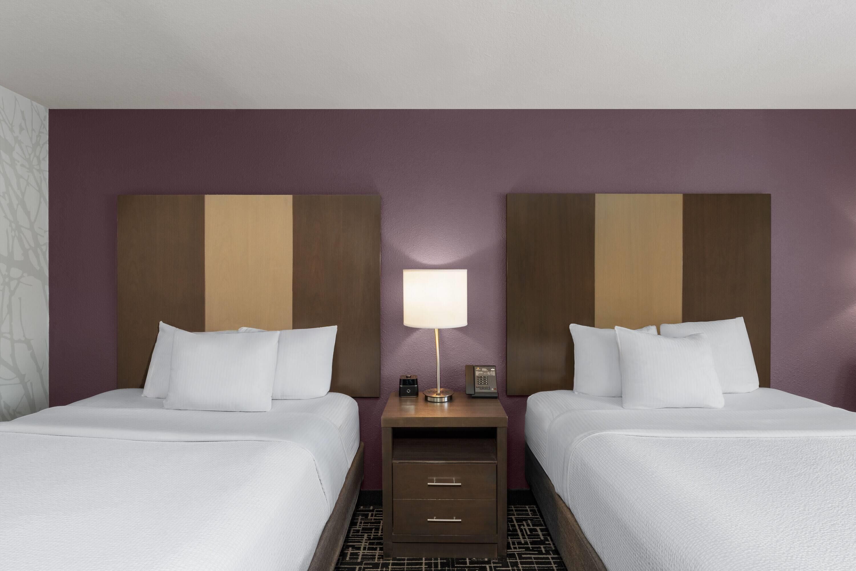 A hotel room with two beds, a nightstand, a lamp, and a small drawer unit.