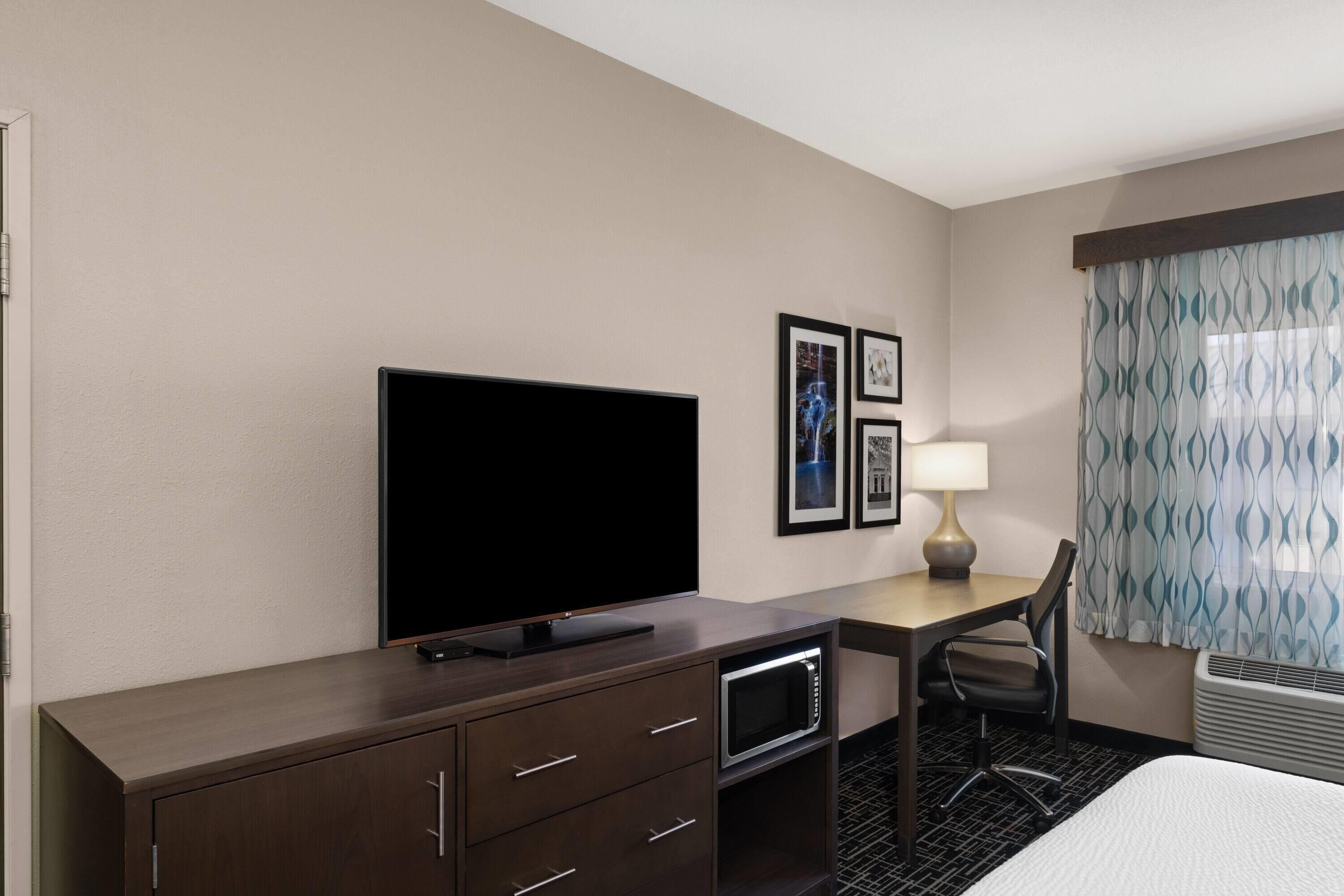 Habitación de hotel con televisor de pantalla plana, escritorio con lámpara, silla y cama.