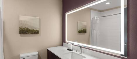 A bathroom with a white sink, a large mirror, a toilet, and a shower.