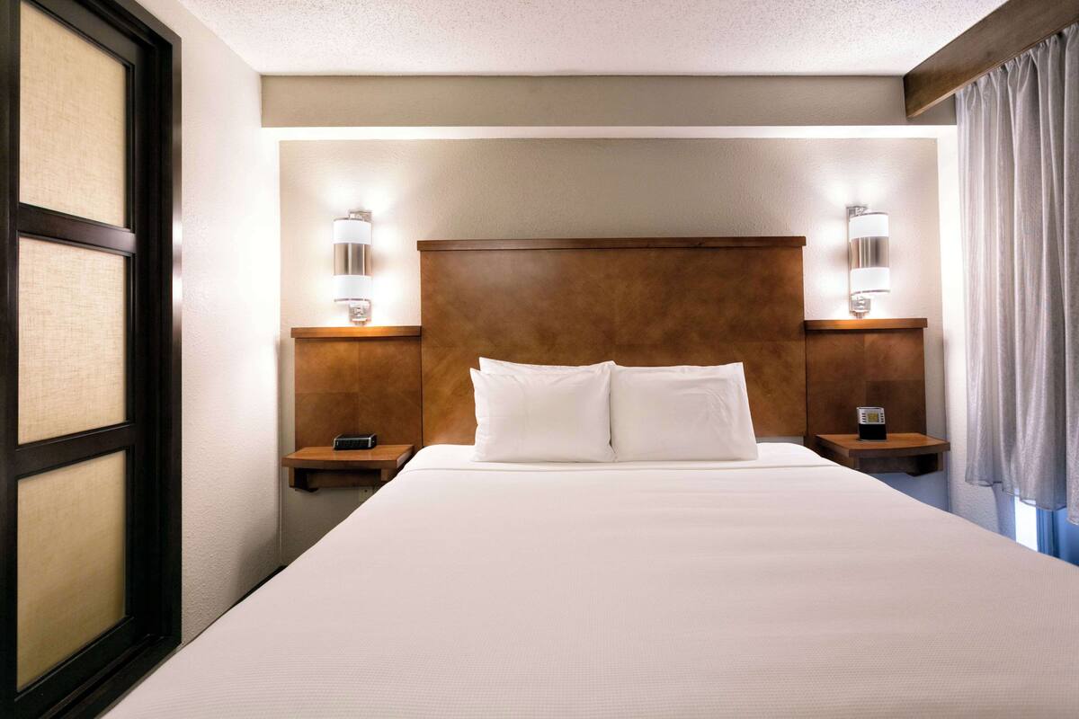 A hotel room with a large bed, two bedside tables, and wall-mounted lamps.