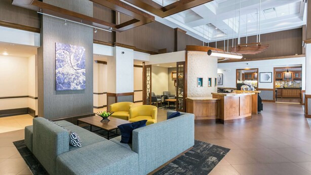 A spacious lobby with a grey sofa, yellow chairs, a coffee table, and a kitchen area in the background. - Hyatt Place Nashville/Franklin/Cool Springs (Franklin)