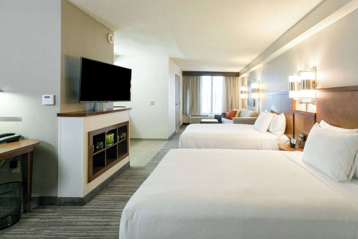 A hotel room with two beds, a TV, a desk with a computer, and a minibar.