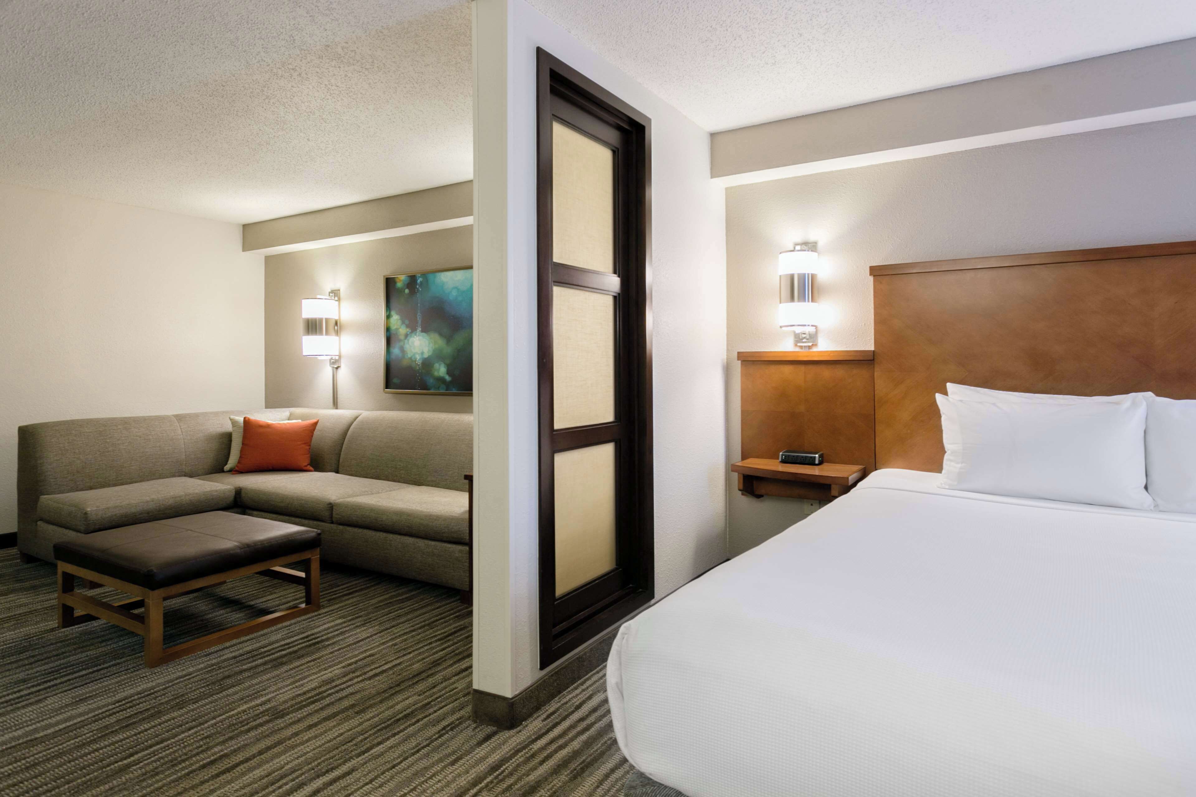 Una habitación de hotel con cama, sofá, una mesita y una lámpara en la mesilla.