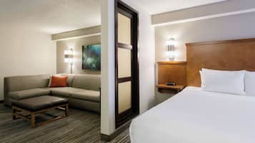 Quarto de hotel com cama, sofá, mesa pequena e mesa de cabeceira com abajur.