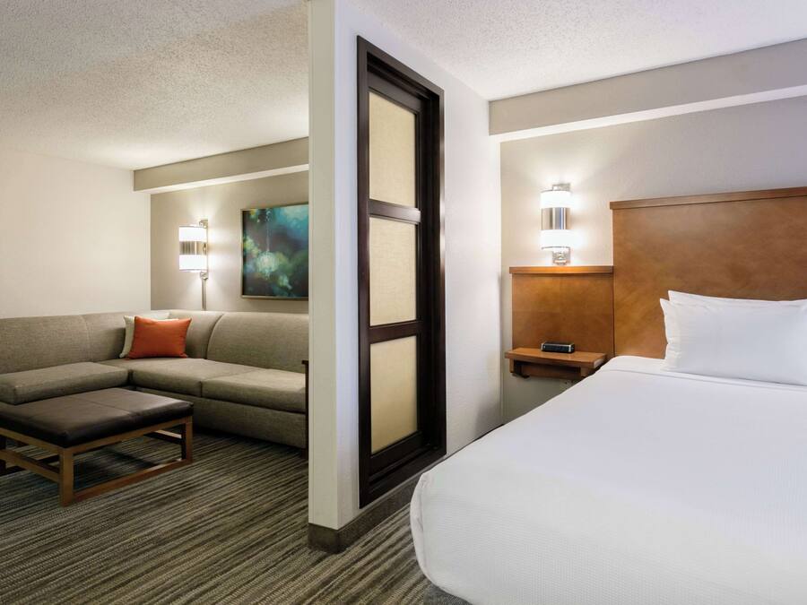 Quarto de hotel com cama, sofá, mesa pequena e mesa de cabeceira com abajur.