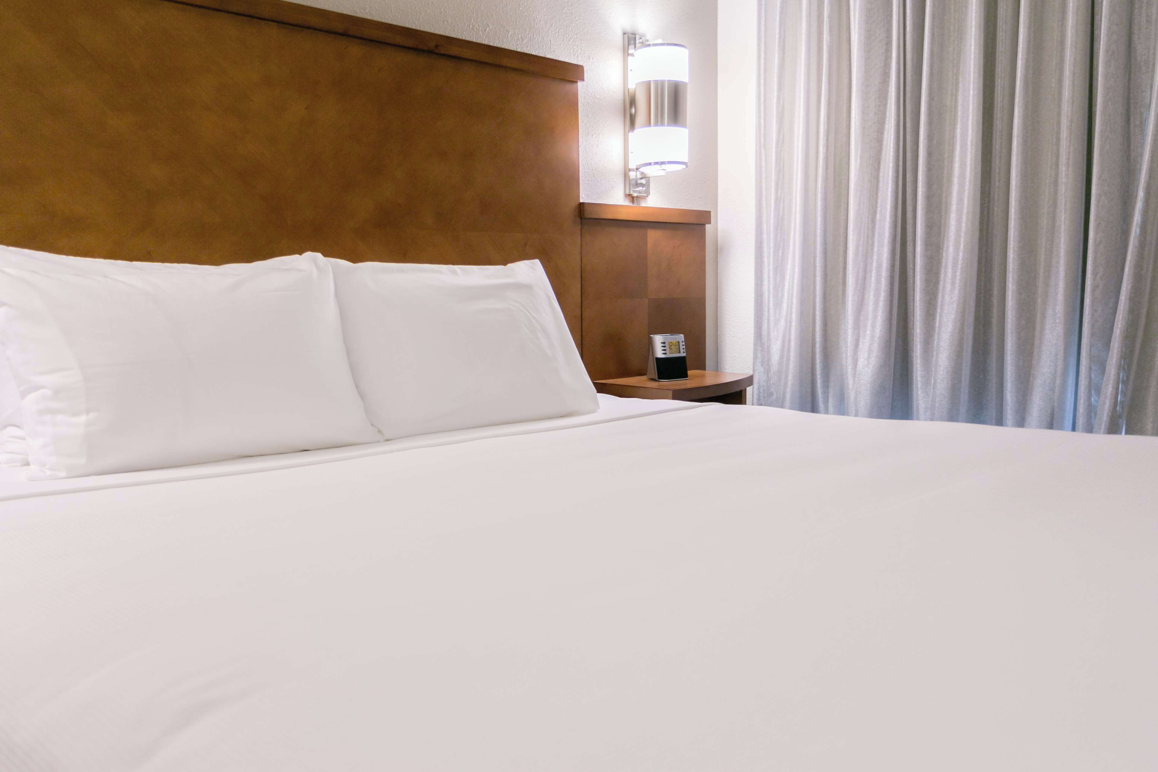 Une chambre d’hôtel avec un grand lit, une tête de lit en bois, une table de chevet avec une lampe et une fenêtre avec des rideaux.