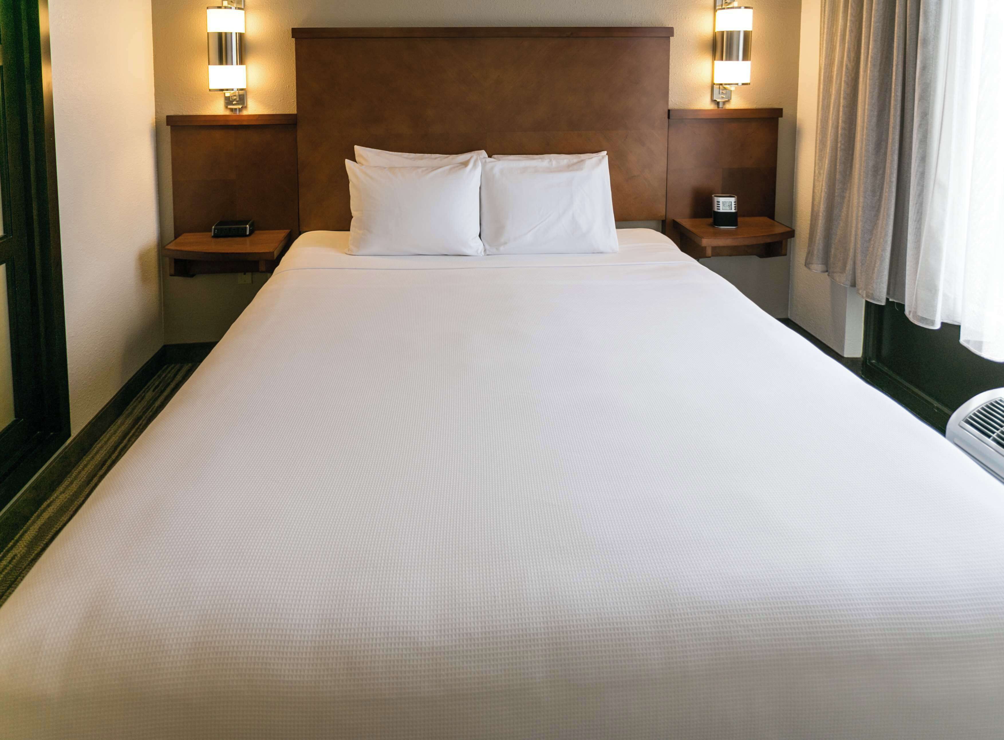 A hotel room with a large bed, two bedside tables, and two wall-mounted lamps.