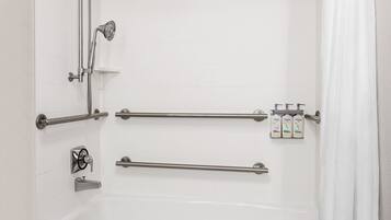 A bathroom with a bathtub, grab bars, a showerhead, and toiletries.