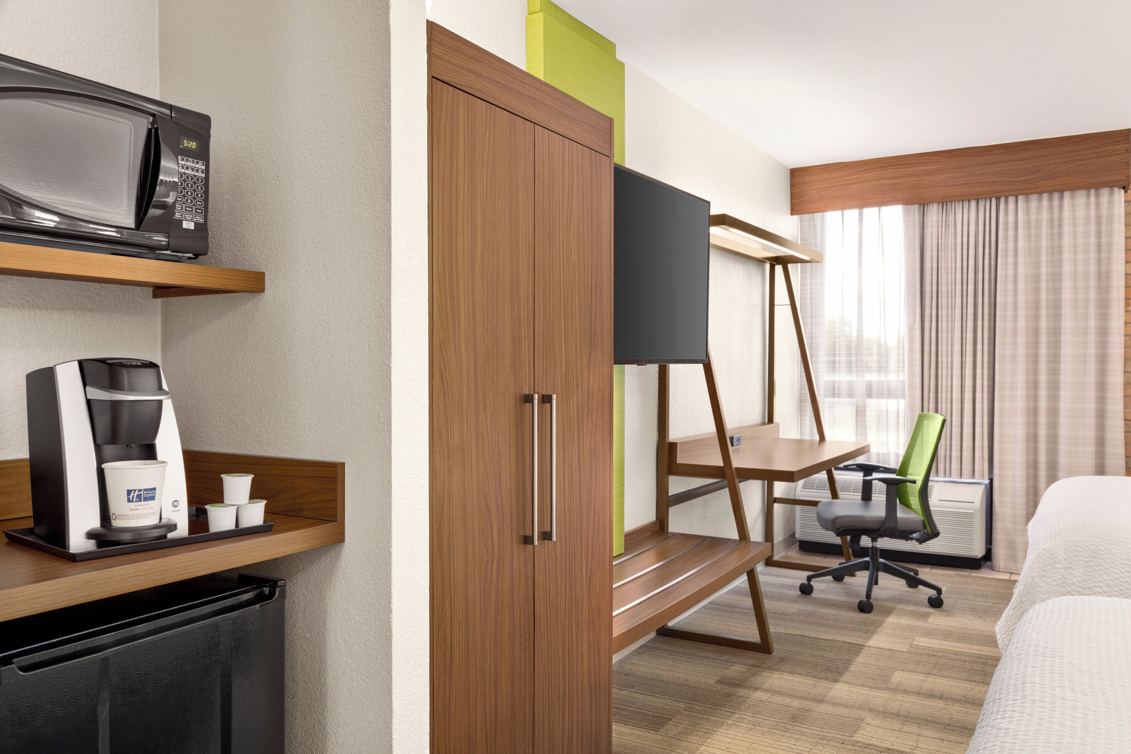 A hotel room with a bed, a desk, a coffee maker, a microwave, and a wardrobe.