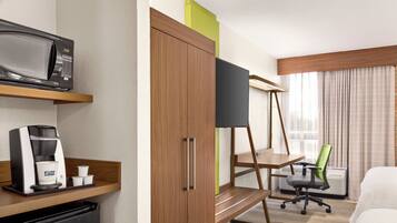 A hotel room with a bed, a desk, a coffee maker, a microwave, and a wardrobe.