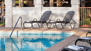 Un área junto a la piscina con sillas de descanso y una baranda de metal.