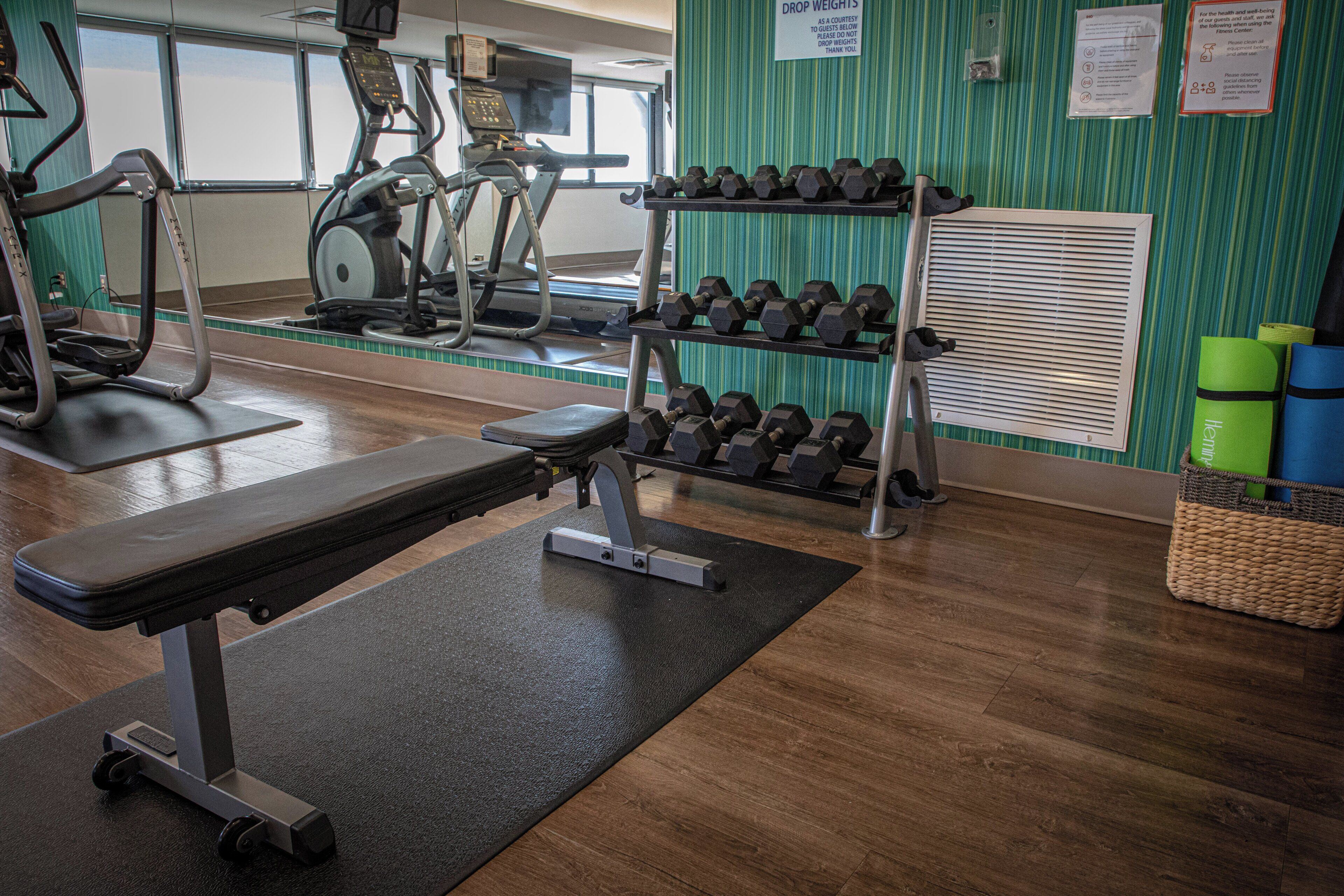 A gym with exercise equipment, a bench, and a rack of dumbbells.