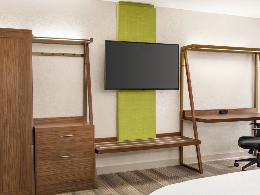 Una habitación con un armario de madera, un escritorio con silla y televisor montado.