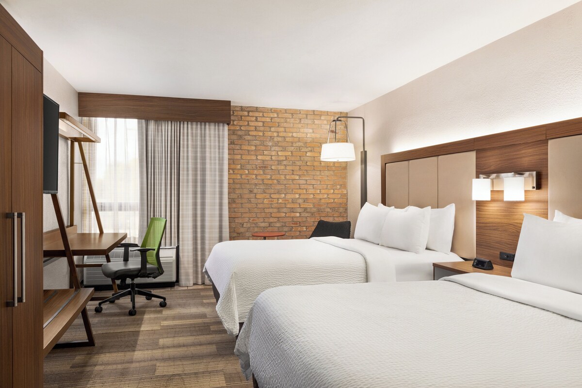 Ein Hotelzimmer mit zwei Betten, einem Schreibtisch, einem Stuhl und einer Wand mit Backsteinverkleidung.