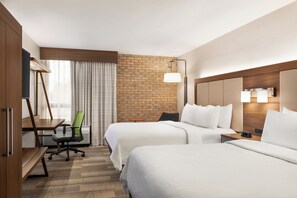 A hotel room with two beds, a desk, a chair, and a brick accent wall.