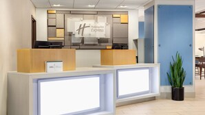 A Holiday Inn Express reception desk with a modern design, featuring a large illuminated sign, a reception area, and a potted plant. - Holiday Inn Express San Antonio-Airport by IHG (San Antonio)