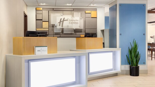Un mostrador de recepción de Holiday Inn Express con un diseño moderno, que incluye un gran letrero iluminado, un área de recepción y una planta en maceta.