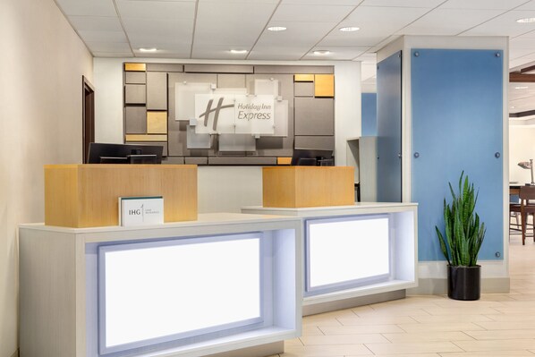 Un mostrador de recepción de Holiday Inn Express con un diseño moderno, que incluye un gran letrero iluminado, un área de recepción y una planta en maceta.