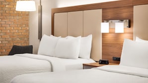 Ein Hotelzimmer mit Backsteinwand, einem Holz-Kopfteil, zwei Betten mit weißer Bettwäsche, einem Nachttisch mit Lampe und einer Wandleuchte.
