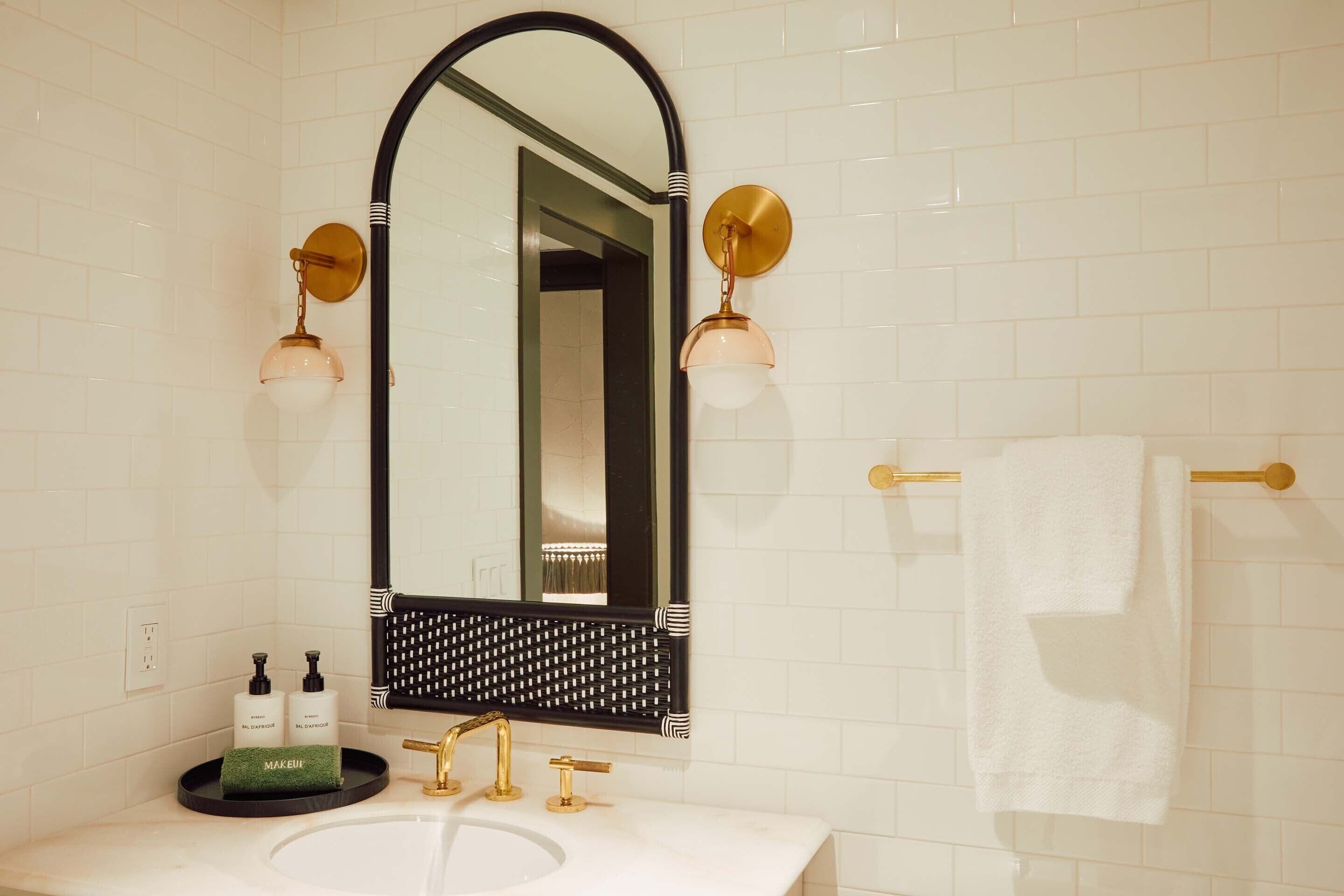 Un baño con lavamanos blanco, accesorios dorados, un espejo grande y dos luces empotradas.