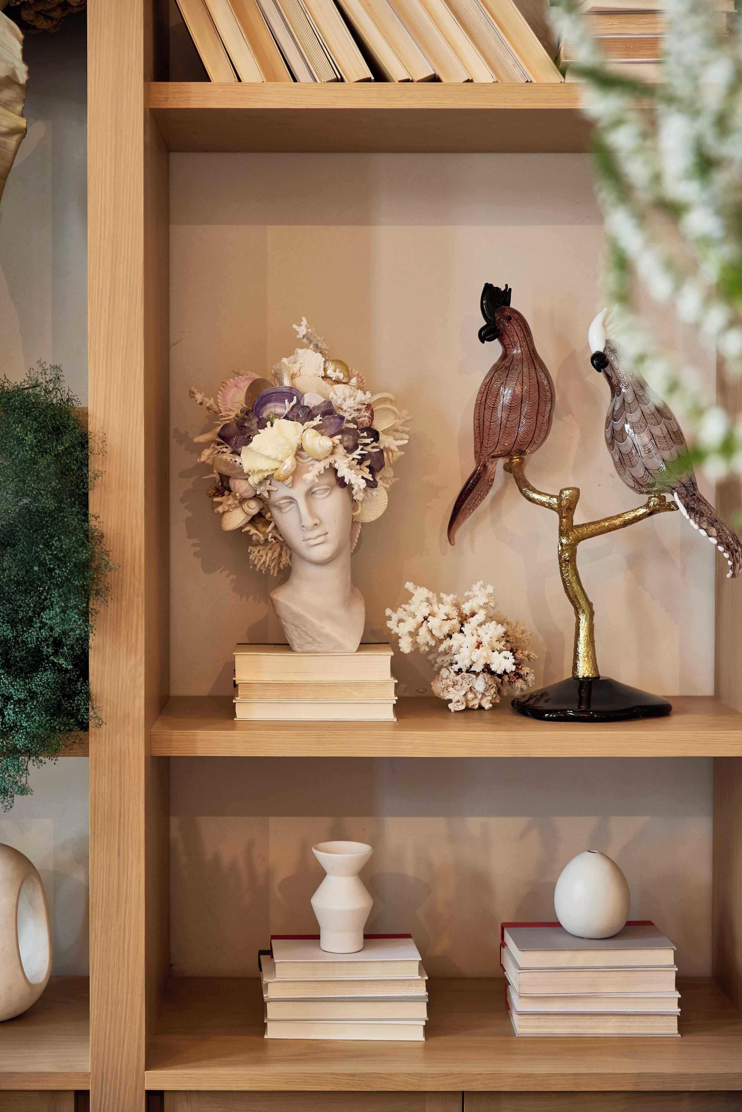 A wooden shelf with decorative items including a bust, a bird sculpture, and books.