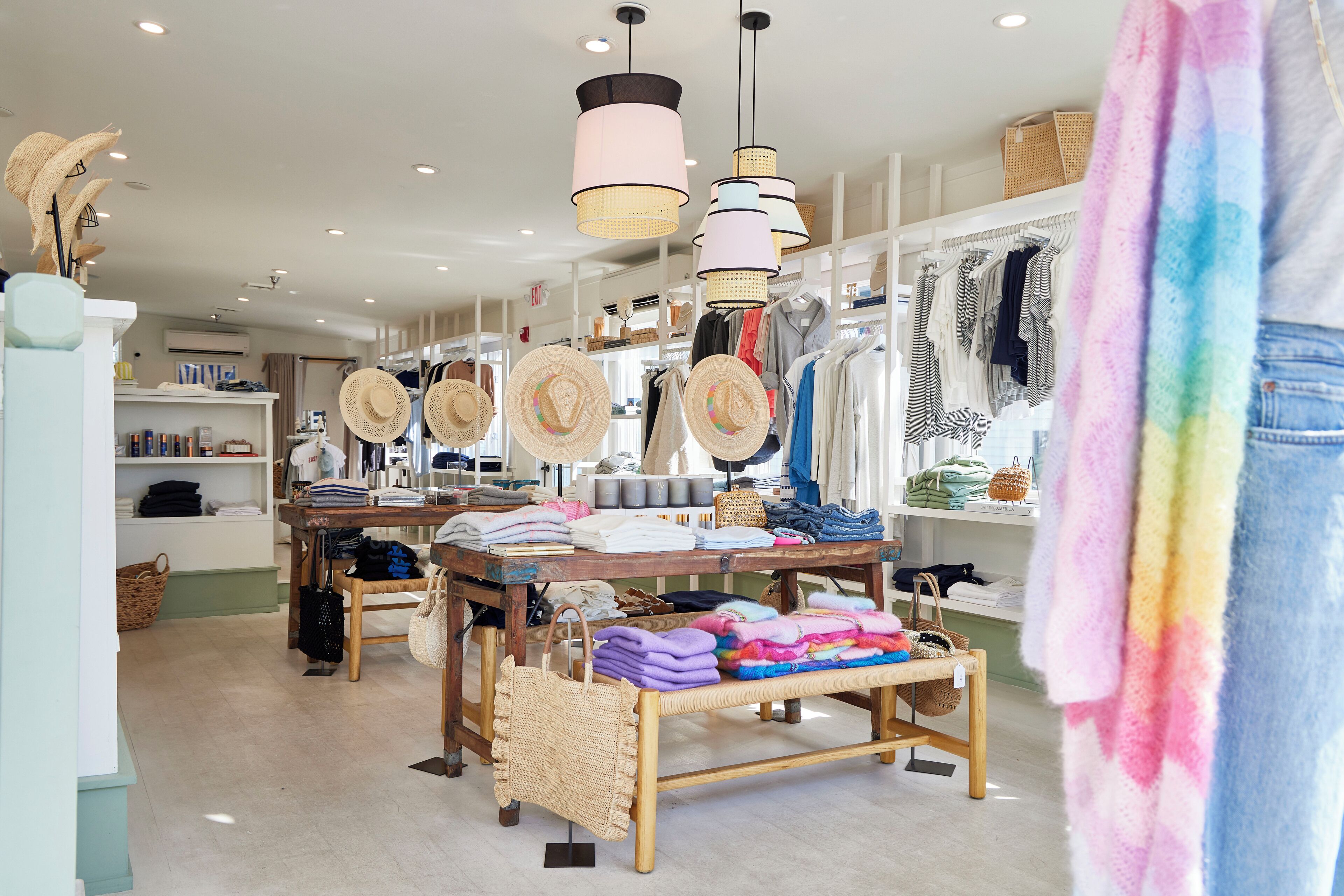 A boutique store with shelves of clothing, a wooden table with folded clothes, and hanging hats.
