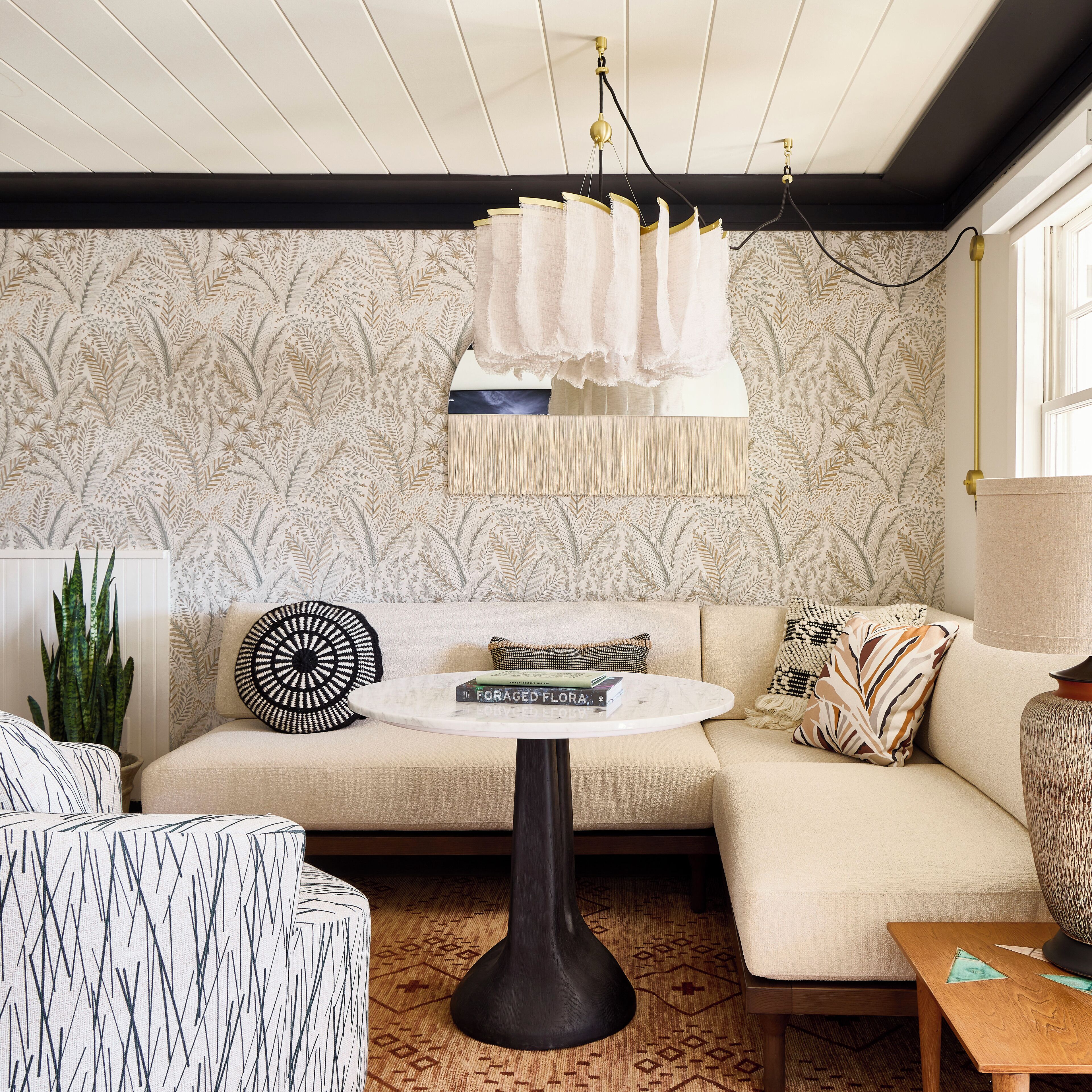 A cozy living room with a patterned wallpaper, a round coffee table, and a modern chandelier.