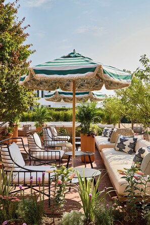 An outdoor seating area with a sofa, chairs, and a table under a striped umbrella. - Faraway Martha's Vineyard (Edgartown)