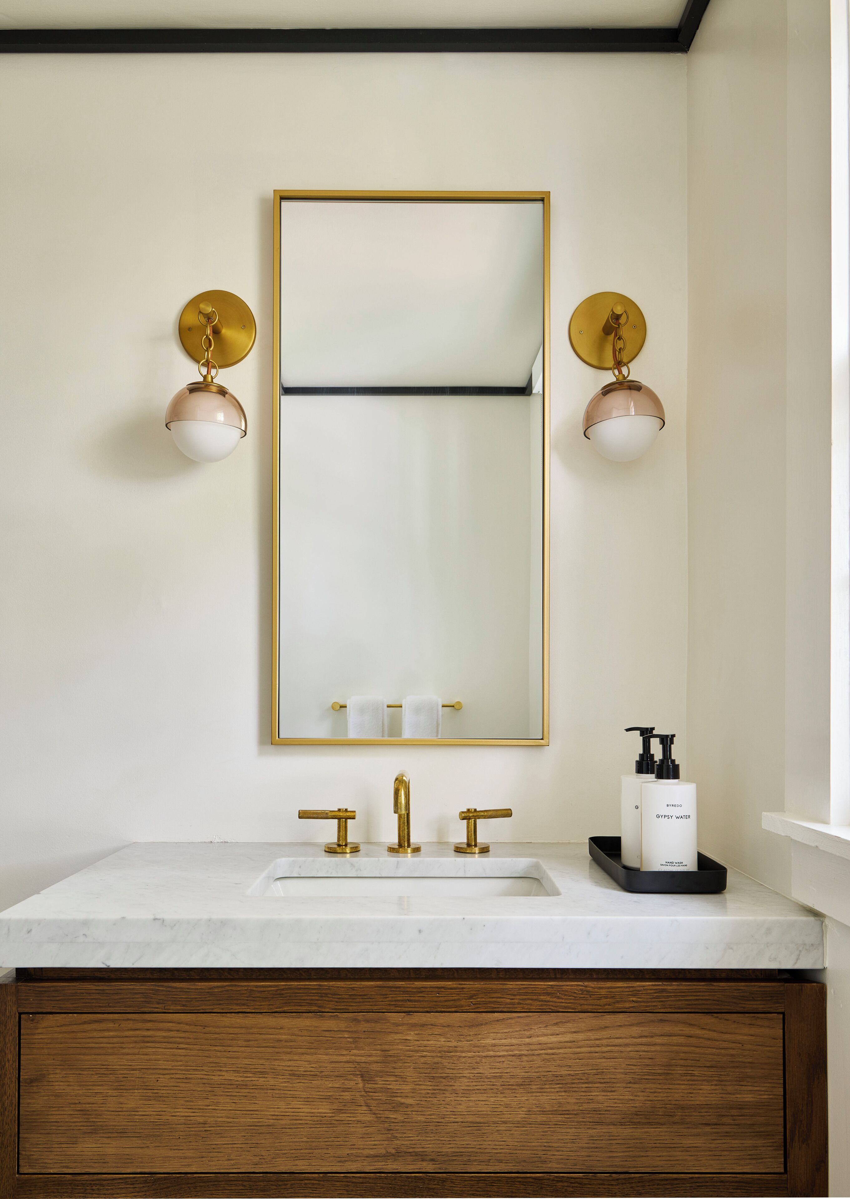 A bathroom with a white marble sink, gold faucets, a gold-framed mirror, and two wall-mounted lights.