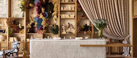 A room with a wooden floor, a round table, a chair, and a bookshelf filled with decorative items.