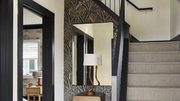 Una escalera con barandilla negra y pared decorada. Se observa un armario de madera con una lámpara encima.