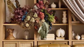 Una sala de estar con un sofá, una estantería y un arreglo floral grande.