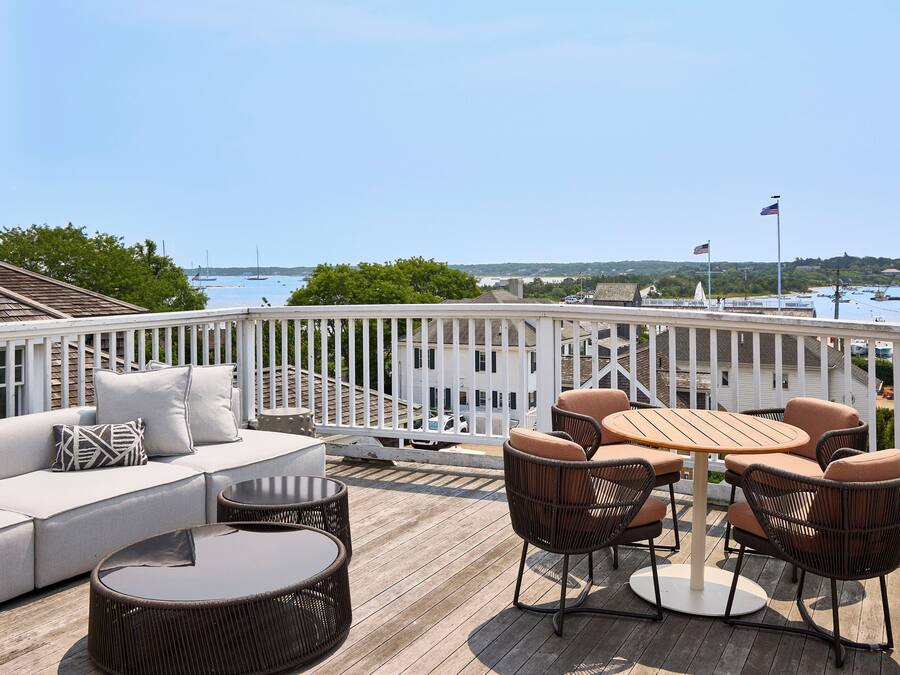 Une terrasse dotée d’un canapé, de chaises et d’une table, offrant une vue sur une marina avec des bateaux et un ciel dégagé.